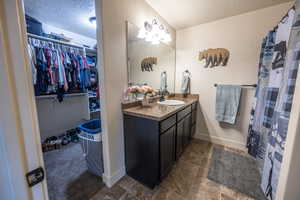 Full bath featuring a walk in closet, baseboards, a textured ceiling, and vanity