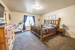 Bedroom with a textured ceiling, dark carpet, and baseboards