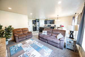 Carpeted living area featuring a textured ceiling, a barn door, recessed lighting, and an inviting chandelier