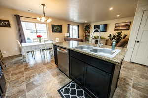 Kitchen featuring decorative light fixtures, a kitchen island with sink, a sink, dark cabinetry, and dishwasher