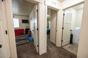 Hall featuring washer / dryer, light colored carpet, visible vents, and a textured ceiling