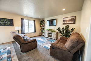 Living room with baseboards, visible vents, a textured ceiling, and recessed lighting