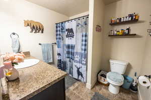 Bathroom with a textured ceiling, toilet, vanity, baseboards, and a shower with curtain