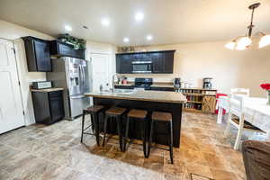 Kitchen with a breakfast bar, stainless steel appliances, a sink, an island with sink, and light stone countertops