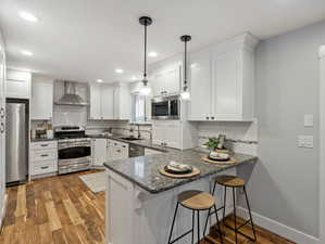 Kitchen featuring white cabinetry, sink, pendant lighting, wall chimney exhaust hood, and stainless steel appliances