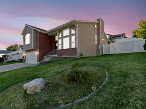 Property exterior at dusk with a garage and a lawn