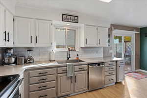 Kitchen with backsplash, white cabinets, stainless steel appliances, and light hardwood / wood-style floors