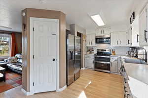 Kitchen featuring white cabinetry, appliances with stainless steel finishes, sink, and light wood-type flooring