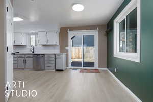 Kitchen featuring white cabinetry, dishwasher, sink, backsplash, and light hardwood / wood-style flooring