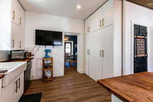 Kitchen with white cabinetry, backsplash, dark wood-type flooring, and stainless steel dishwasher