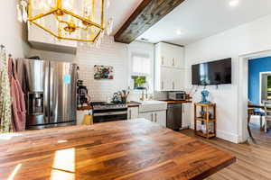 Kitchen with beam ceiling, stainless steel appliances, pendant lighting, white cabinetry, and light hardwood / wood-style floors