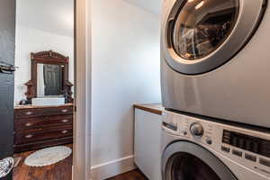 Washroom with stacked washing maching and dryer, dark hardwood / wood-style floors, and sink