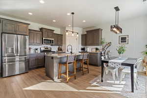 Kitchen with appliances with stainless steel finishes, light hardwood / wood-style flooring, dark brown cabinetry, and tasteful backsplash