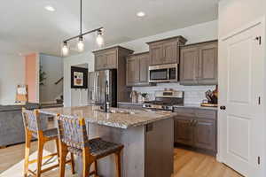 Kitchen featuring hanging light fixtures, stainless steel appliances, sink, light wood-type flooring, and light stone counters