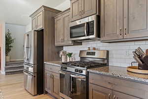 Kitchen with stone countertops, stainless steel appliances, light hardwood / wood-style flooring, and backsplash