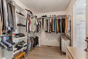 Walk in closet with light hardwood / wood-style floors