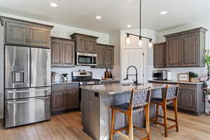 Kitchen with decorative backsplash, sink, light wood-type flooring, appliances with stainless steel finishes, and light stone counters