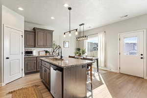 Kitchen with dark brown cabinets, light hardwood / wood-style flooring, stainless steel dishwasher, and a center island with sink