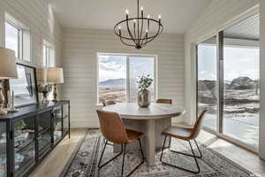 Dining area with an inviting chandelier, wooden walls, vaulted ceiling, and light wood-type flooring