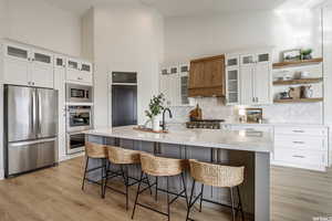 Kitchen featuring white cabinetry, high vaulted ceiling, stainless steel appliances, and a center island with sink