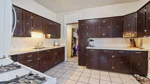 Kitchen featuring light tile patterned flooring, dark brown cabinetry, sink, and white gas stove