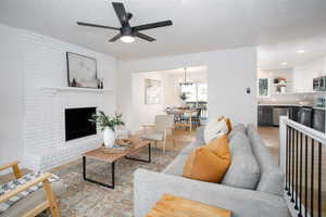 Living room featuring a textured ceiling, light hardwood / wood-style flooring, a brick fireplace, and ceiling fan with notable chandelier