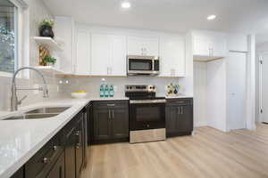 Kitchen featuring light stone countertops, appliances with stainless steel finishes, sink, light wood-type flooring, and white cabinets