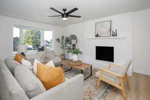 Living room featuring light hardwood / wood-style floors, a textured ceiling, a fireplace, and ceiling fan