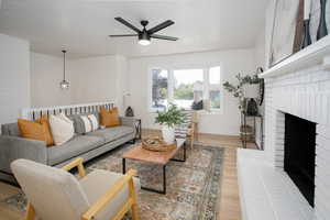 Living room with light hardwood / wood-style floors, a textured ceiling, a brick fireplace, and ceiling fan