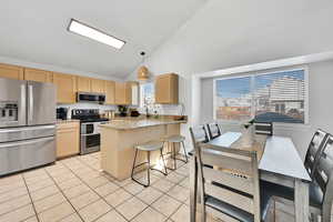 Kitchen with light stone counters, light brown cabinets, stainless steel appliances, and decorative light fixtures