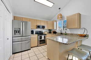 Kitchen with light brown cabinets, appliances with stainless steel finishes, decorative light fixtures, kitchen peninsula, and a breakfast bar area