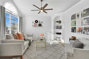 Carpeted living room with vaulted ceiling, built in features, and ceiling fan