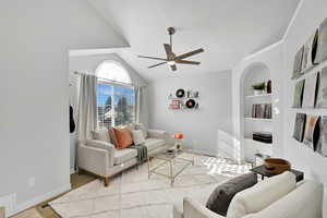 Living room featuring built in shelves, ceiling fan, and vaulted ceiling