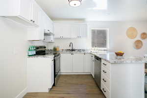 Kitchen with white cabinets, appliances with stainless steel finishes, hardwood / wood-style flooring, light stone countertops, and sink