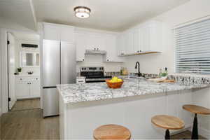 Kitchen featuring kitchen peninsula, appliances with stainless steel finishes, white cabinets, and sink