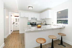 Kitchen featuring light stone countertops, electric range, light hardwood / wood-style flooring, and white cabinetry