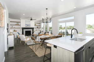 Kitchen featuring dishwasher, a kitchen island with sink, dark wood-type flooring, sink, and decorative light fixtures