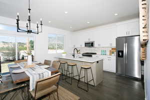 Kitchen featuring appliances with stainless steel finishes, a kitchen island with sink, white cabinets, and dark hardwood / wood-style flooring