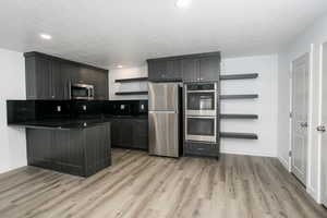 Kitchen featuring appliances with stainless steel finishes, kitchen peninsula, a textured ceiling, and light wood-type flooring