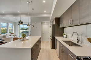 Kitchen featuring stainless steel appliances, sink, pendant lighting, light hardwood / wood-style floors, and tasteful backsplash