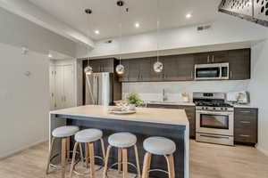 Kitchen with appliances with stainless steel finishes, sink, light wood-type flooring, dark brown cabinets, and decorative light fixtures