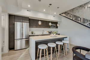 Kitchen with appliances with stainless steel finishes, a kitchen bar, light wood-type flooring, sink, and decorative light fixtures