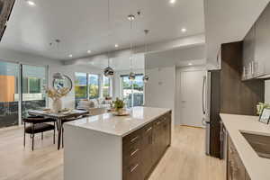 Kitchen with a kitchen island, light wood-type flooring, stainless steel refrigerator, pendant lighting, and sink