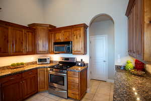 Kitchen featuring dark stone countertops, stainless steel appliances, and light tile patterned floors