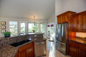 Kitchen with lofted ceiling, appliances with stainless steel finishes, dark stone counters, sink, and decorative light fixtures