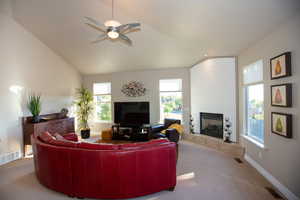 Living room with lofted ceiling, a tiled fireplace, light colored carpet, and ceiling fan