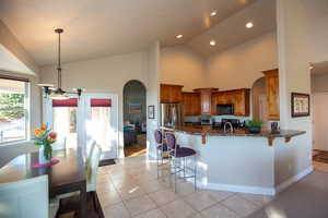 Kitchen featuring a kitchen breakfast bar, light tile patterned flooring, stainless steel appliances, and dark stone counters