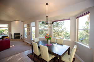 Dining room with vaulted ceiling, light tile patterned flooring, a fireplace, and a wealth of natural light