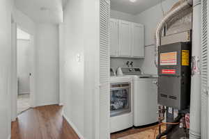 Washroom with separate washer and dryer, hardwood / wood-style floors, heating unit, and cabinets