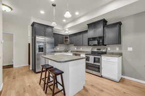 Kitchen featuring a center island, decorative light fixtures, stainless steel appliances, and light wood flooring